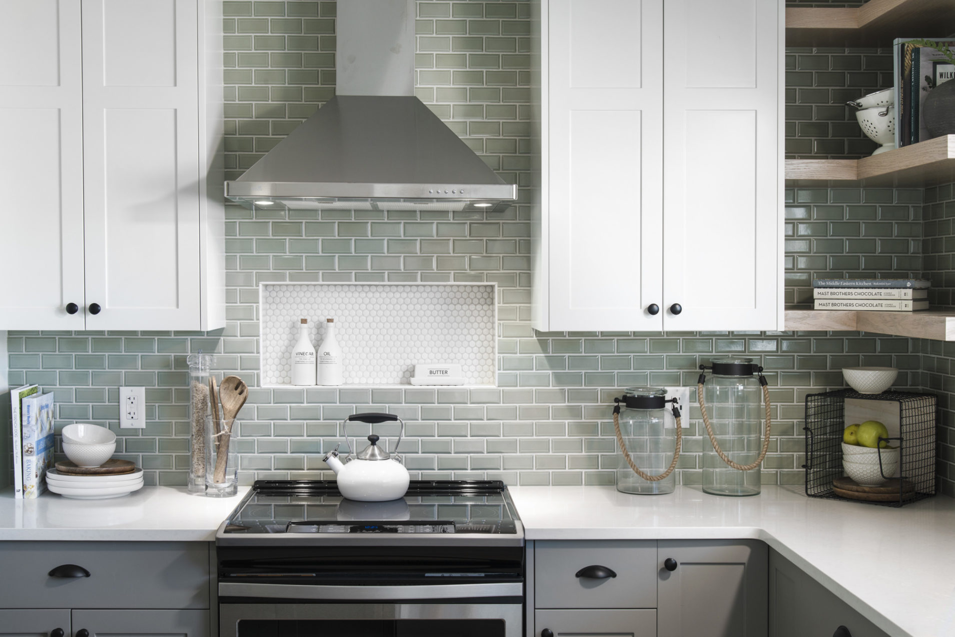 A kitchen with sage green tiles, and grey and white cabinets.