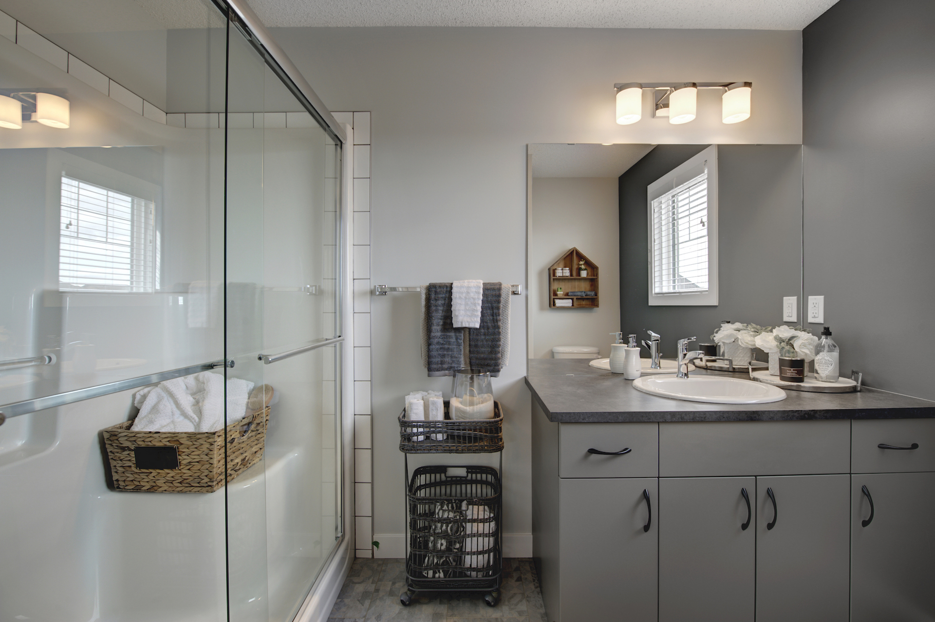 A bathroom with grey cabinets and a glass-walled shower.