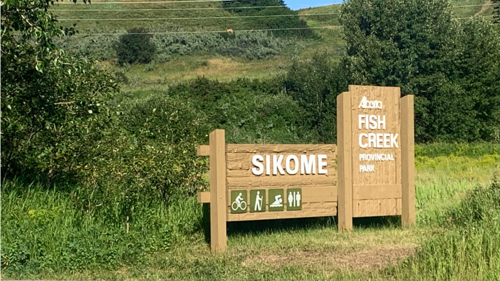 a sign reads Sikome Lake in front of a field of lush, green grass.