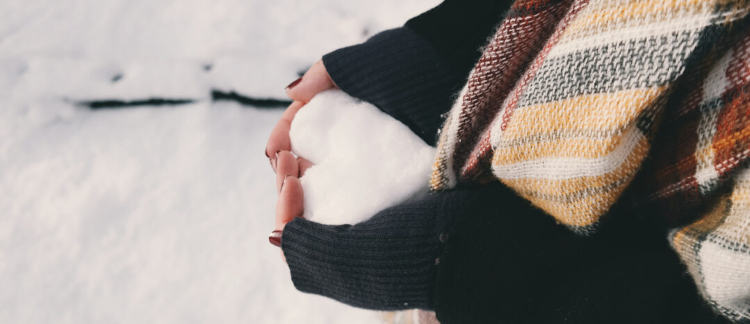 A person wearing a scarf holds a snowball shaped like a heart.