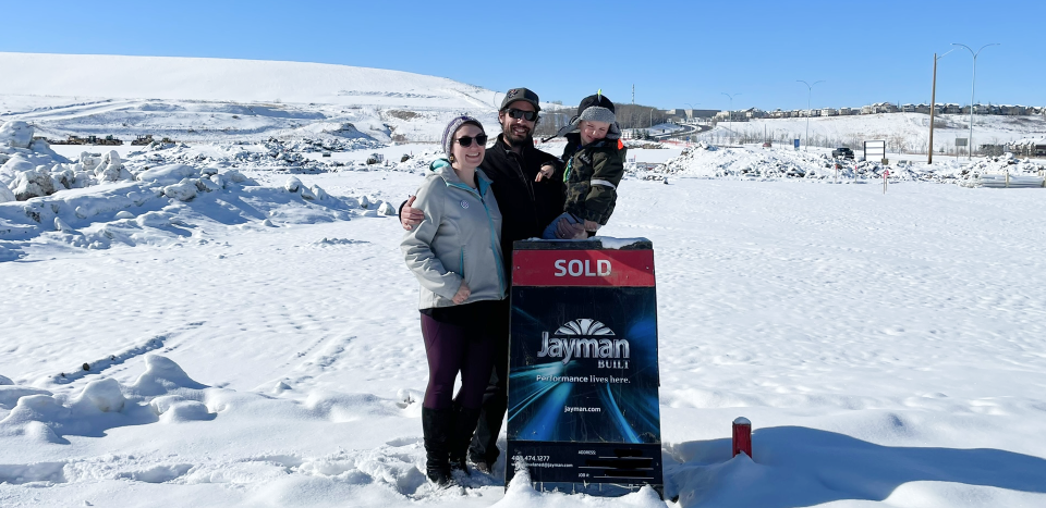 Two adults and a child stand behind a Jayman BUILT sold sign.