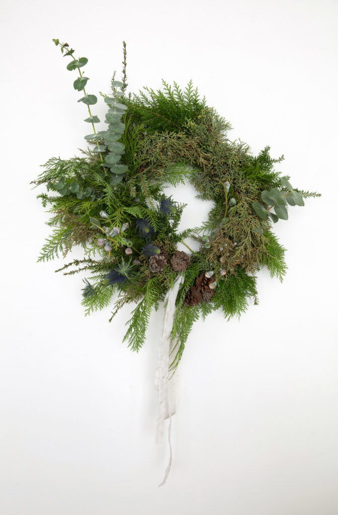 asymmetrical holiday wreath with lots of greenery, pinecones, and ribbon