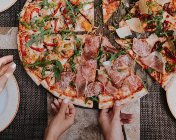 an overhead photo of a pizza and 5 hands reaching in to grab a slice