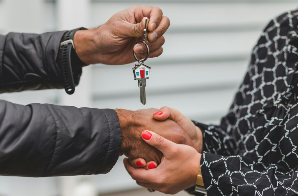 Two people shaking hands while handing over keys to a newly purchased home.