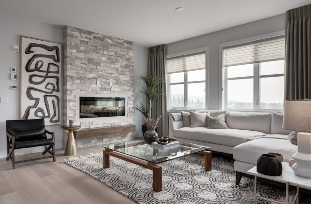 A living room with plush sectional, lots of natural lighting, and an electic fireplace with stone surround.