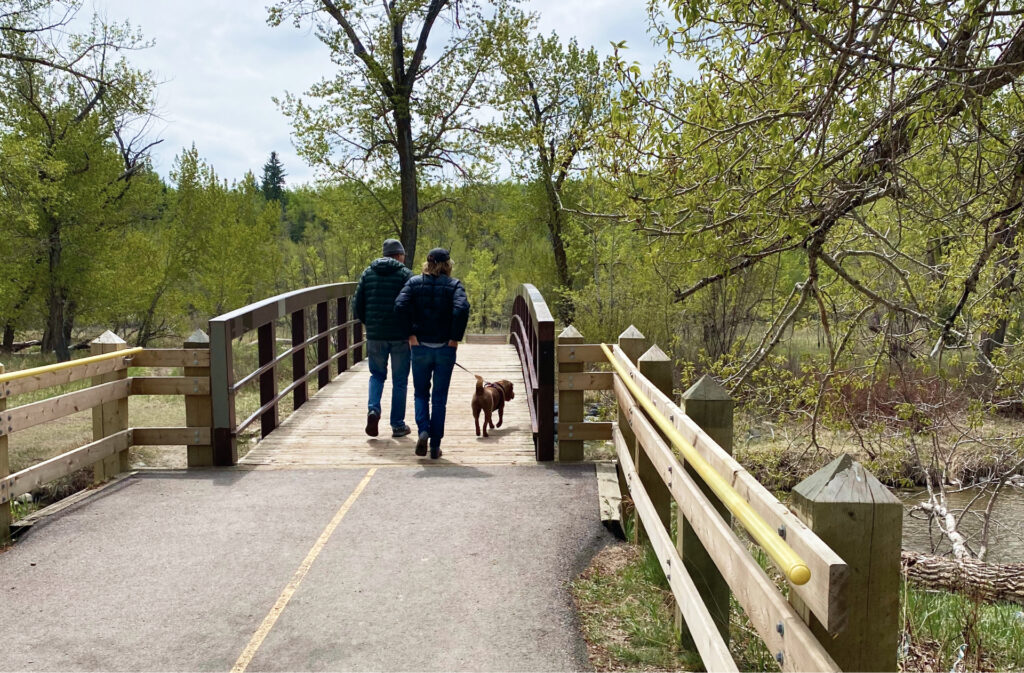 A couple walking their dog in Fish Creek Park on a paved path.