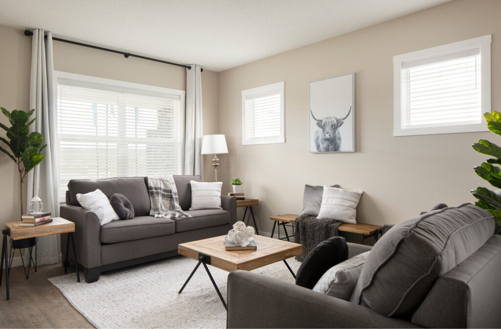 A neutral toned living room, with light beige walls and dark grey couches.