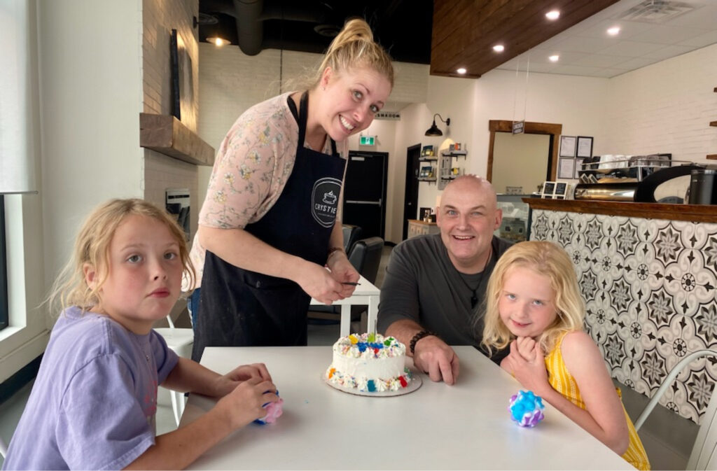 Crystie and her family smiling around a cake in the coffee house.