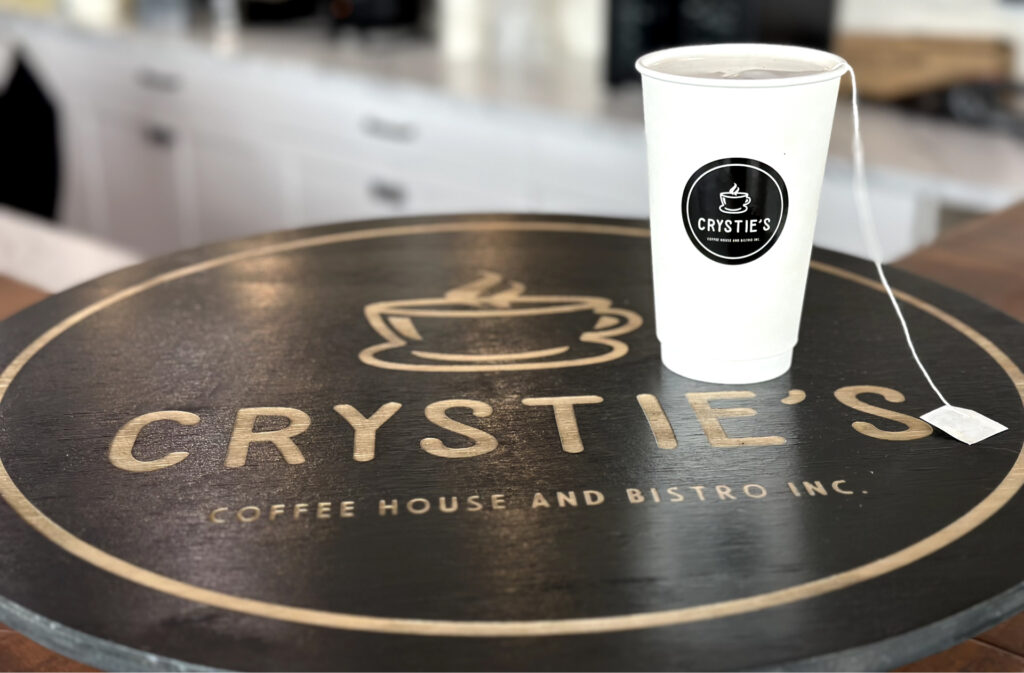 Tea in a to-go cup, sitting on a "Crystie's Coffee" branded board.