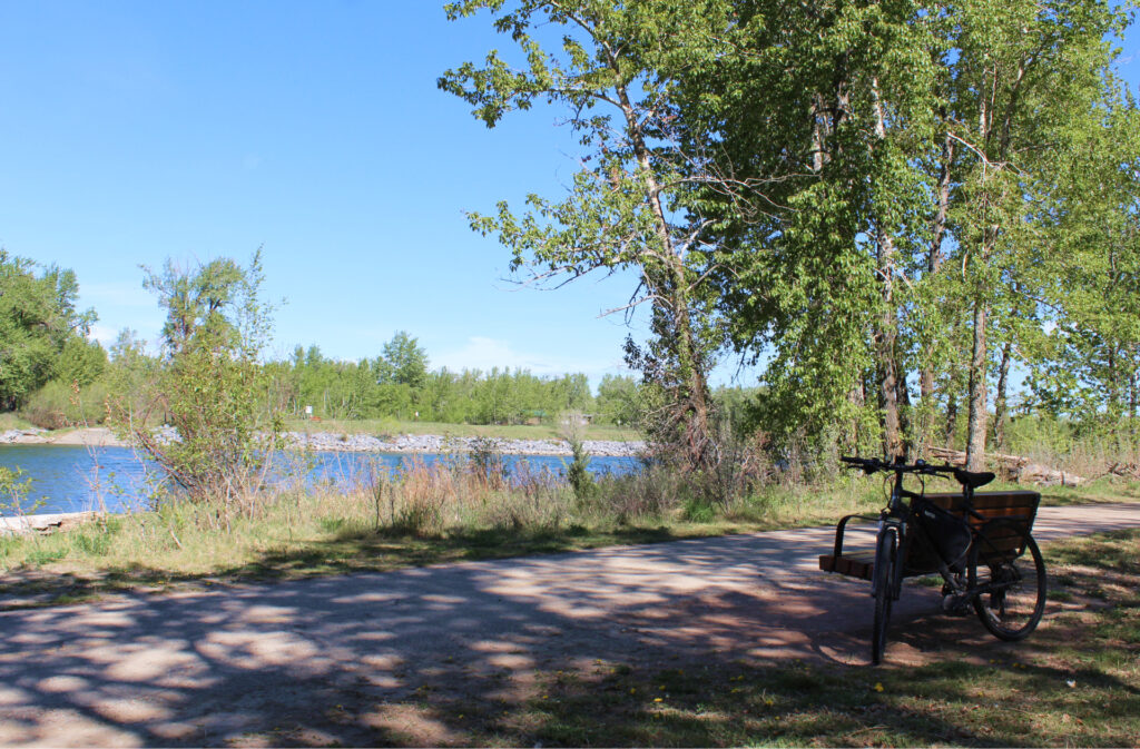 A bike rests against a bench on a path next to the Bow River.