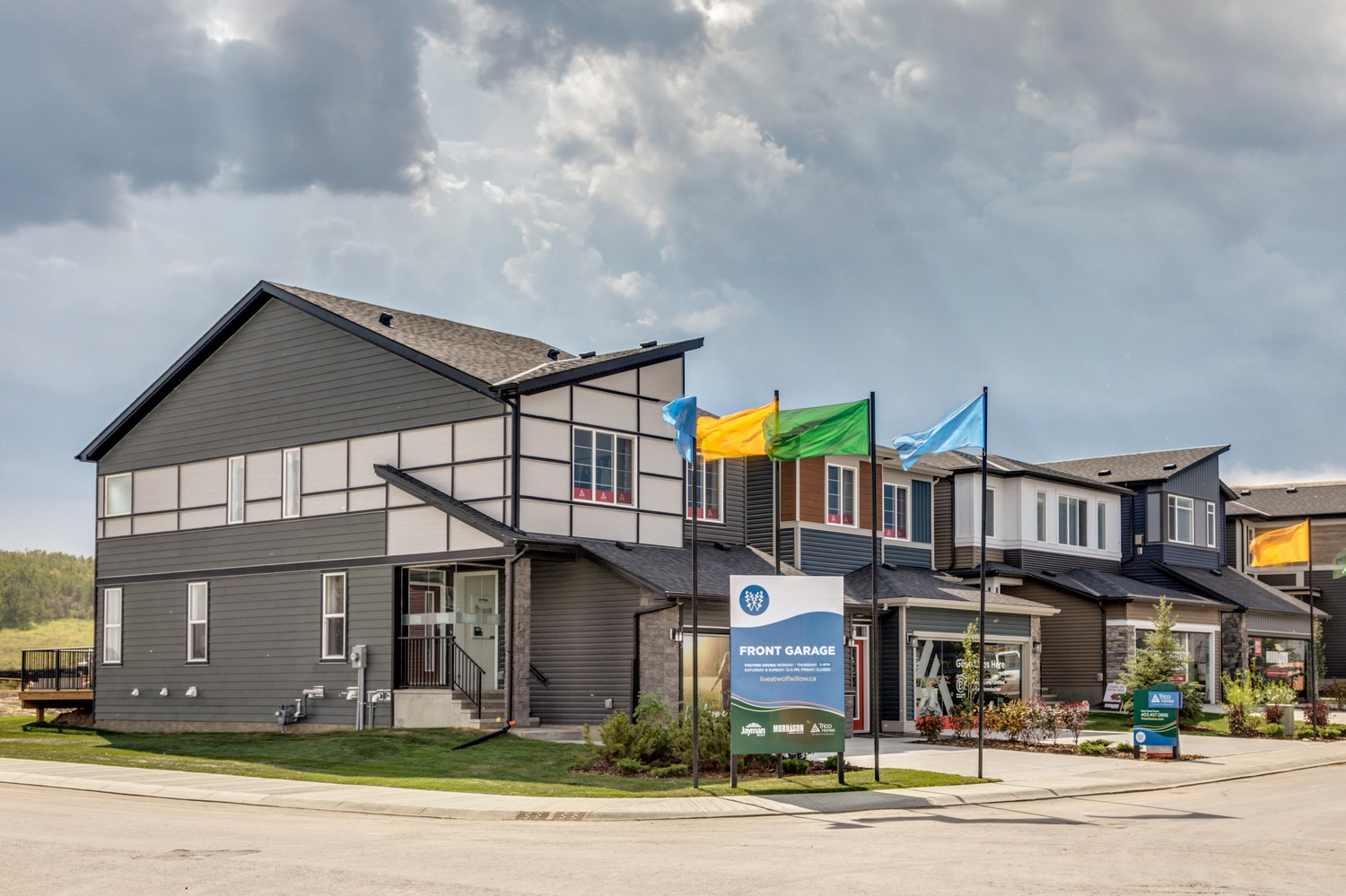 Front garage show homes with a show home sign and blue, green and yellow flags located in Wolf Willow.