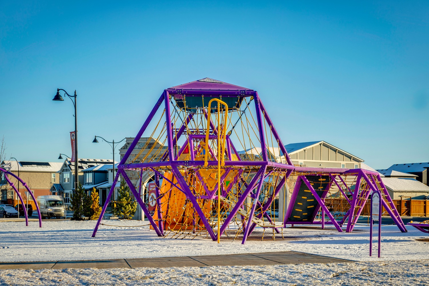 Purple coloured playground with yellow rope walks and climbing holds in the community of Legacy.